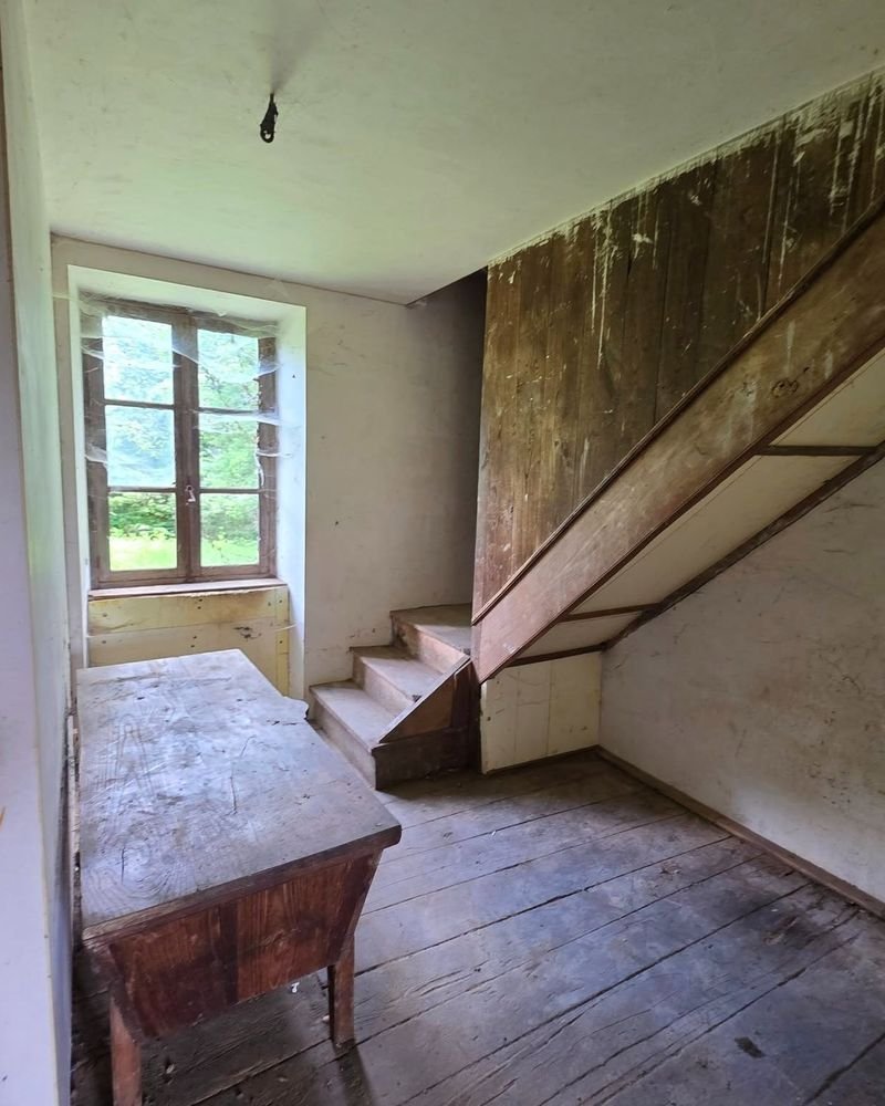 Pièce d'une maison de famille vidée, avec son escalier en bois et sa fenêtre sur le jardin